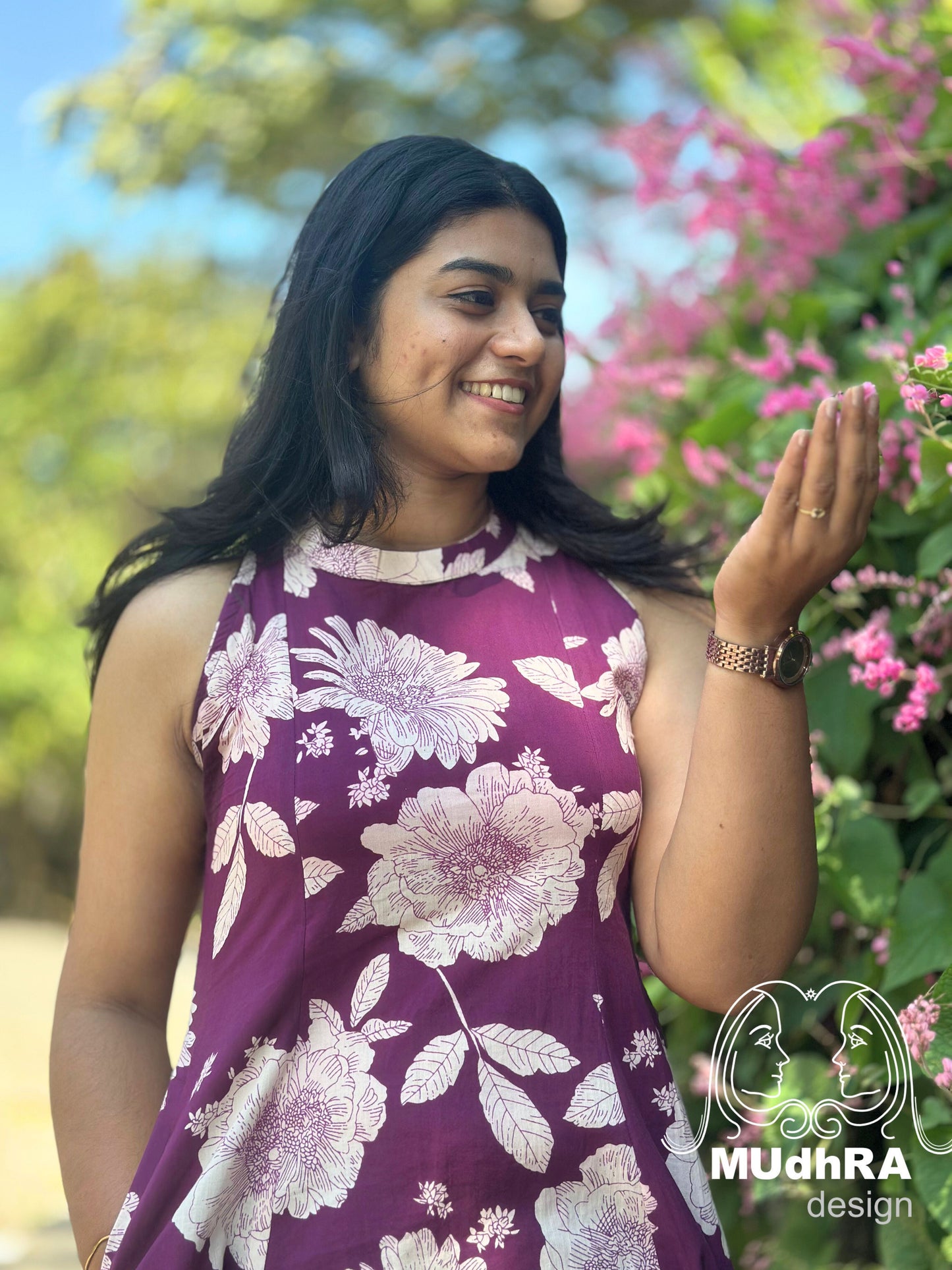 Woman in a floral dress standing outdoors with greenery and flowers in the background
