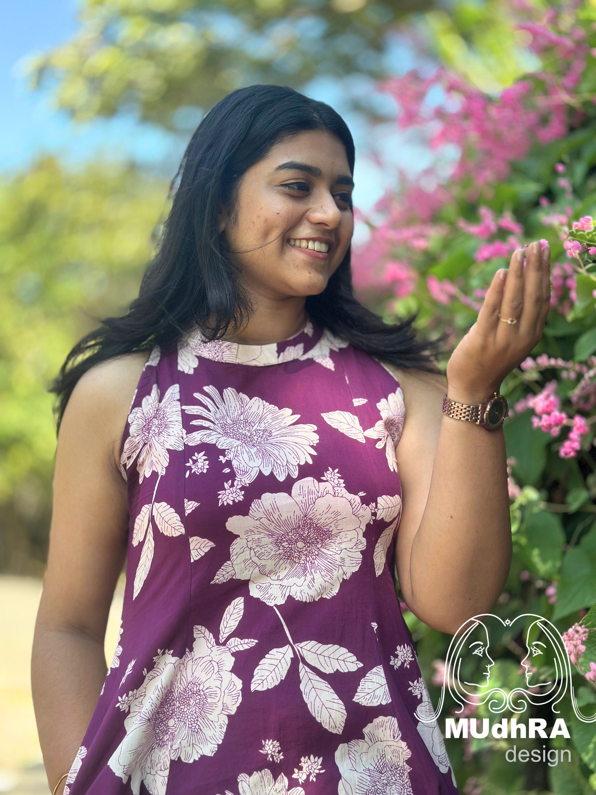 Woman in a floral dress standing outdoors with greenery and flowers in the background