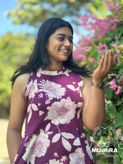 Woman in a floral dress standing outdoors with greenery and flowers in the background